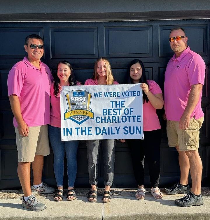 Kuykendall Roofing team holding Best of Charlotte 2022 banner in front of garage door, celebrating local roofing excellence