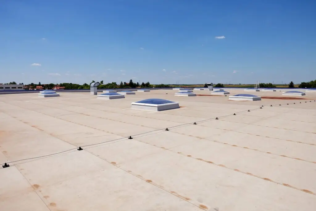 Wide view of a flat commercial roof with white HVAC units and skylights under a clear blue sky.