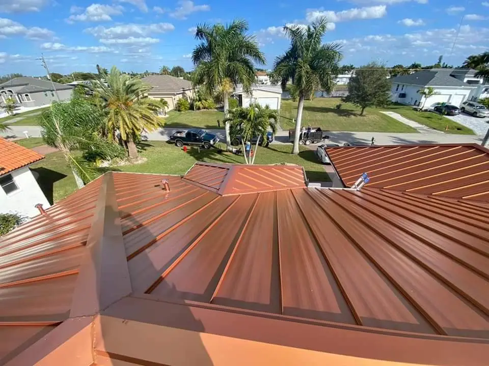 View of a newly installed copper-colored metal roof on a waterfront home in Florida, with palm trees and canal-side houses in the background.
