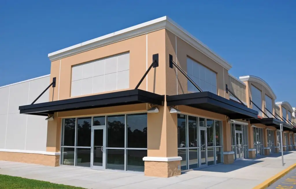 Commercial building with a flat roof and modern tan facade, featuring black awnings and large glass storefronts.