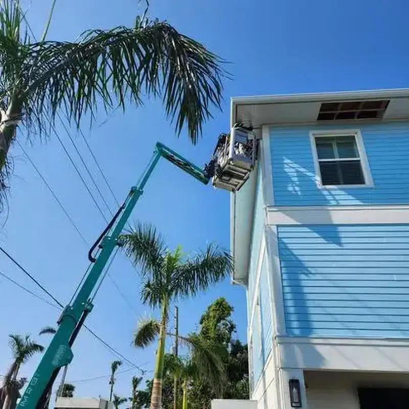 Kuykendall Roofing technician installing gutters and fascia from a hydraulic lift on a blue Florida home